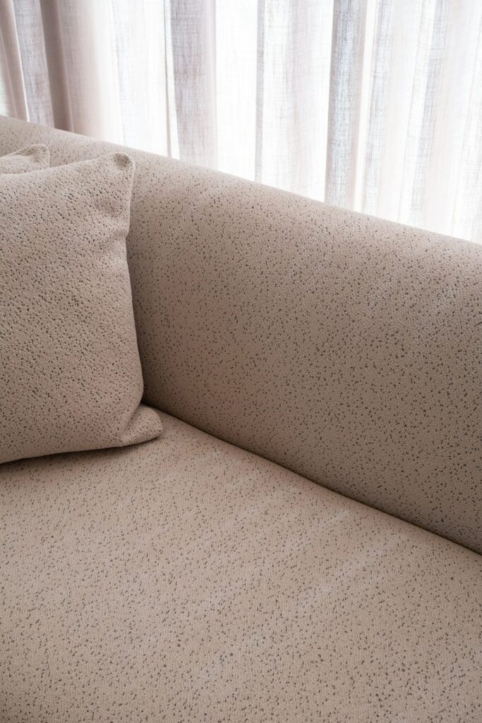 A textured beige sofa with a pillow and curtains